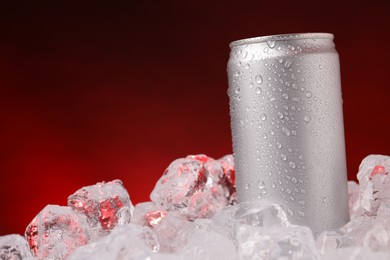 Photo of Refreshing drink in can on ice cubes against dark red background, closeup