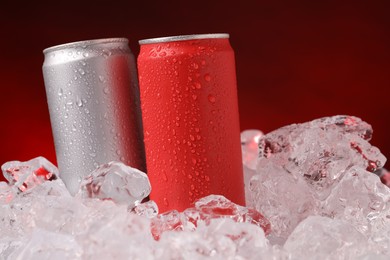 Photo of Refreshing drinks in cans on ice cubes against dark red background, closeup