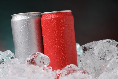 Photo of Refreshing drinks in cans on ice cubes against dark background, closeup