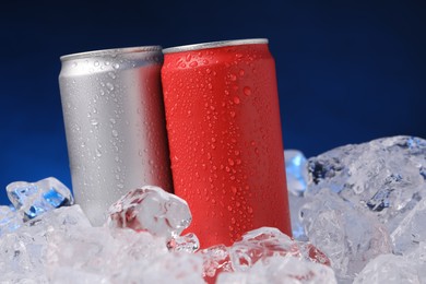 Photo of Refreshing drinks in cans on ice cubes against dark blue background, closeup