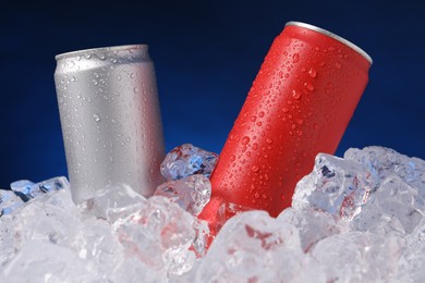 Photo of Refreshing drinks in cans on ice cubes against dark blue background, closeup