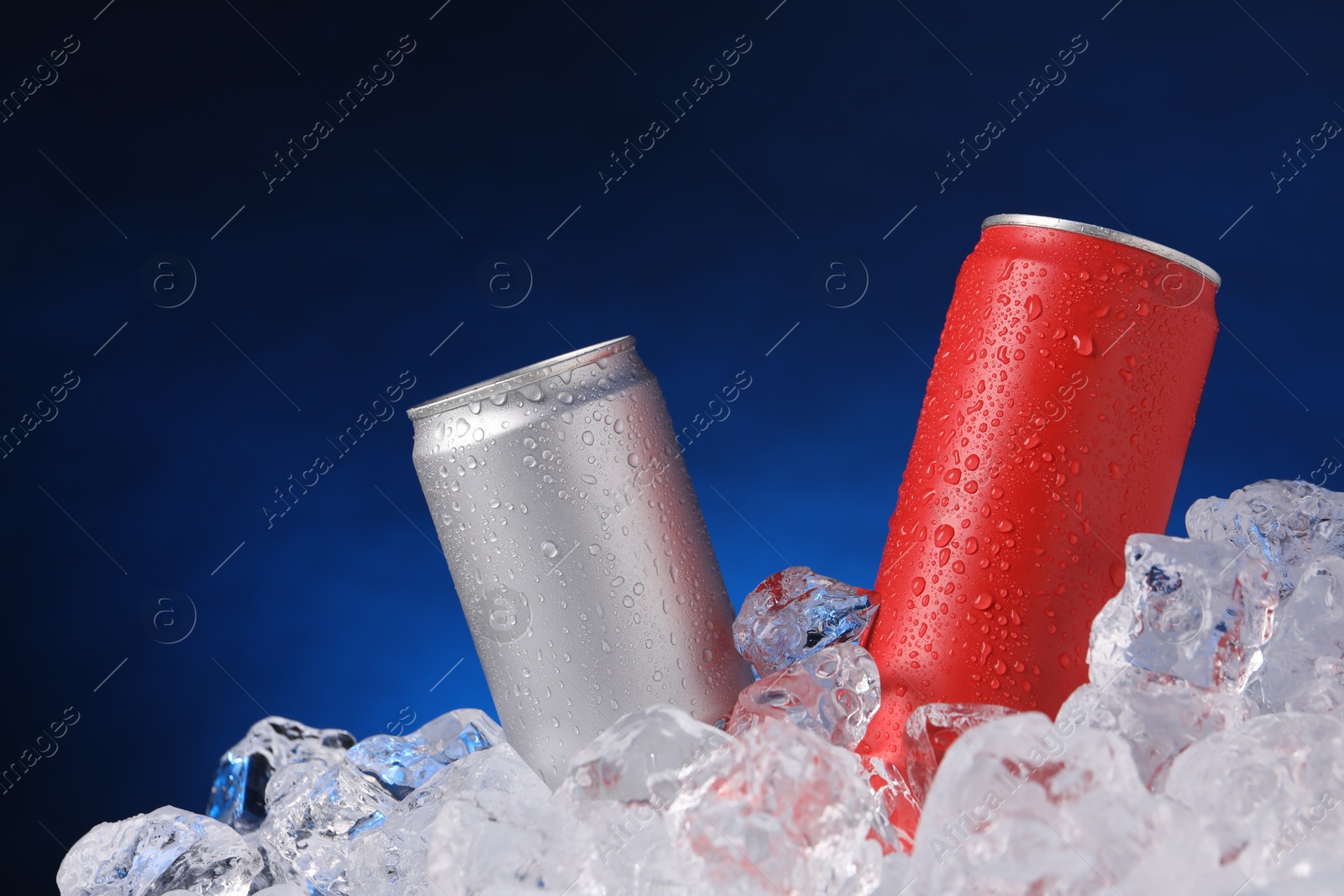 Refreshing drinks in cans on ice cubes against dark blue background Photo of Refreshing drinks in cans on ice cubes against dark blue background
