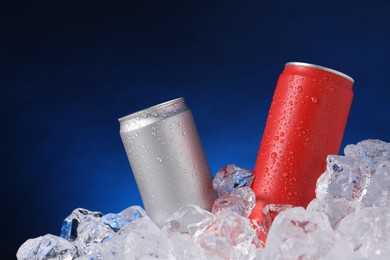 Photo of Refreshing drinks in cans on ice cubes against dark blue background