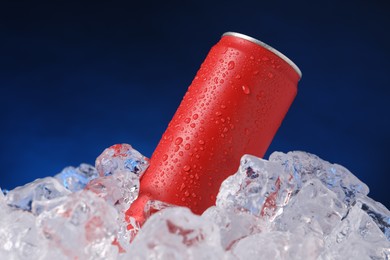Photo of Refreshing drink in can on ice cubes against dark blue background