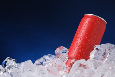 Photo of Refreshing drink in can on ice cubes against dark blue background