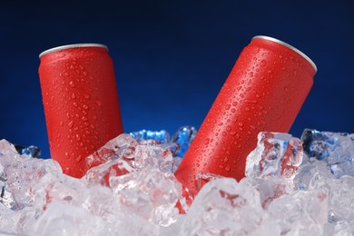 Photo of Refreshing drinks in cans on ice cubes against dark blue background, closeup