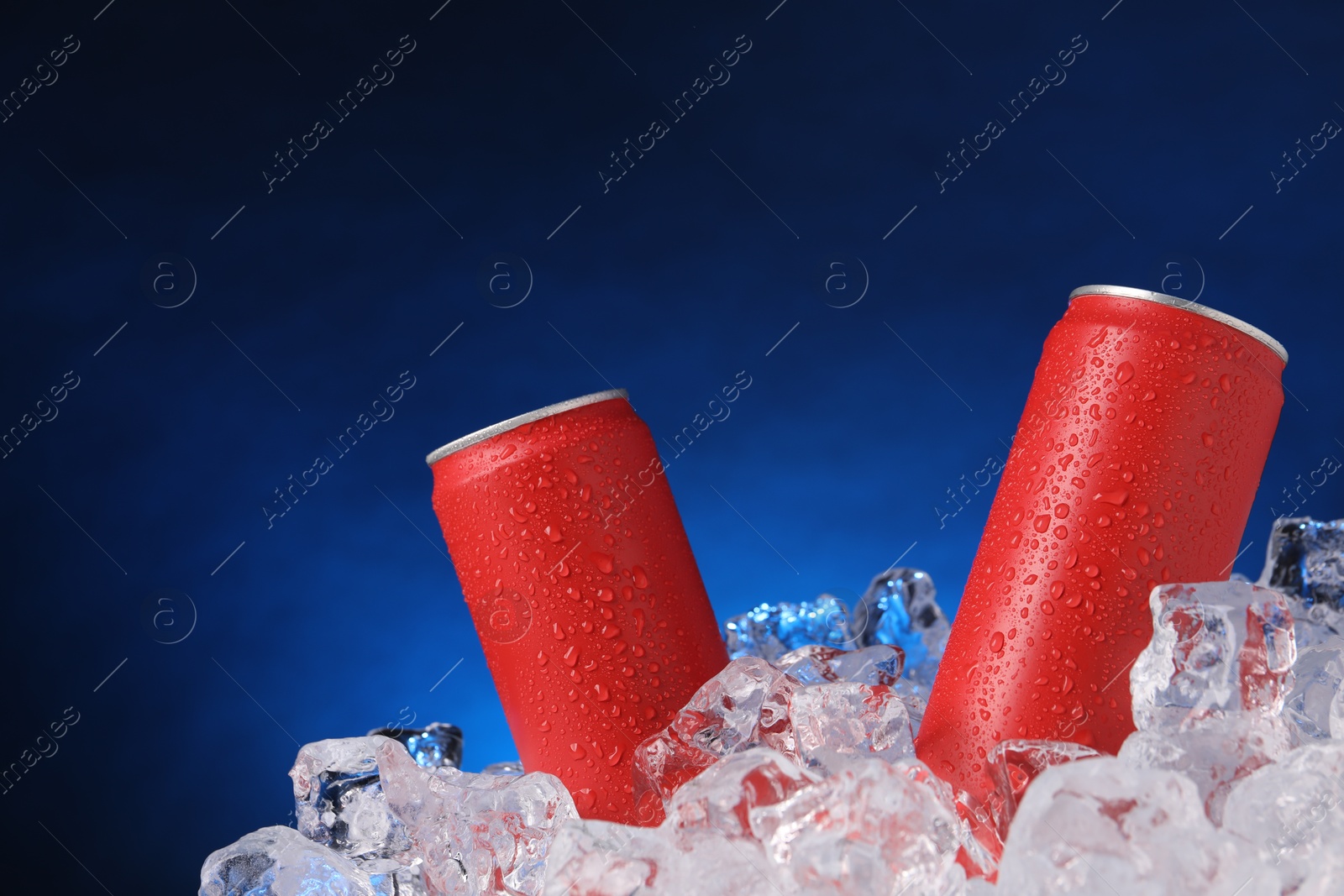 Refreshing drinks in cans on ice cubes against dark blue background Photo of Refreshing drinks in cans on ice cubes against dark blue background