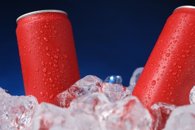 Photo of Refreshing drinks in cans on ice cubes against dark blue background, closeup