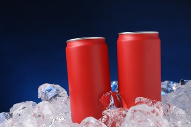 Photo of Refreshing drinks in cans on ice cubes against dark blue background
