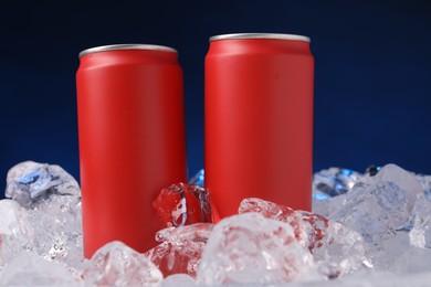 Photo of Refreshing drinks in cans on ice cubes against dark blue background, closeup