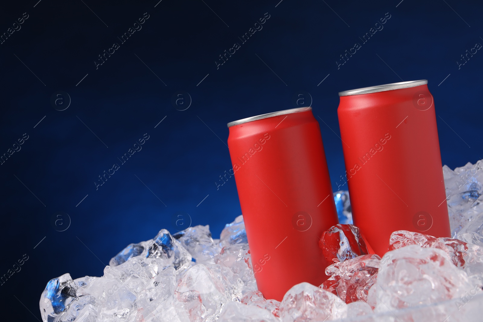 Refreshing drinks in cans on ice cubes against dark blue background Photo of Refreshing drinks in cans on ice cubes against dark blue background