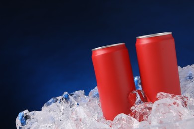Photo of Refreshing drinks in cans on ice cubes against dark blue background