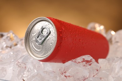 Photo of Refreshing drink in can on ice cubes against golden background, closeup