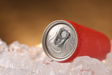 Photo of Refreshing drink in can on ice cubes against golden background, closeup