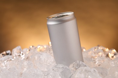 Photo of Refreshing drink in can on ice cubes against golden background, closeup