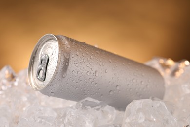 Photo of Refreshing drink in can on ice cubes against golden background, closeup