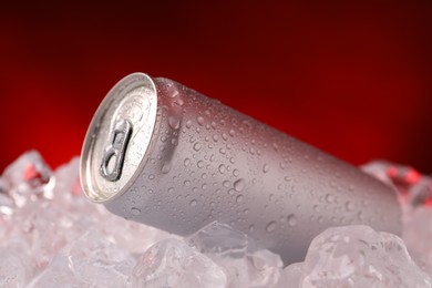 Photo of Refreshing drink in can on ice cubes against dark red background, closeup