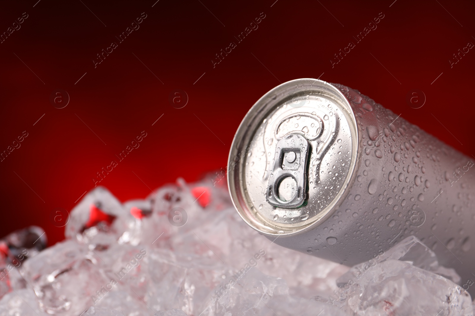 Refreshing drink in can on ice cubes against dark red background, closeup Photo of Refreshing drink in can on ice cubes against dark red background, closeup