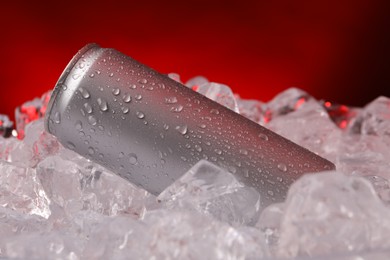 Photo of Refreshing drink in can on ice cubes against dark red background, closeup