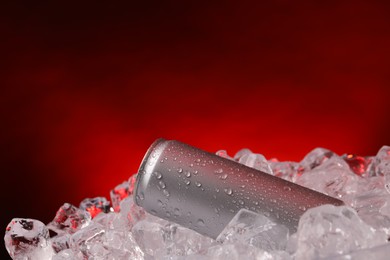 Photo of Refreshing drink in can on ice cubes against dark red background, closeup