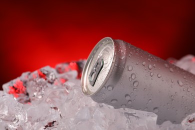 Photo of Refreshing drink in can on ice cubes against dark red background, closeup