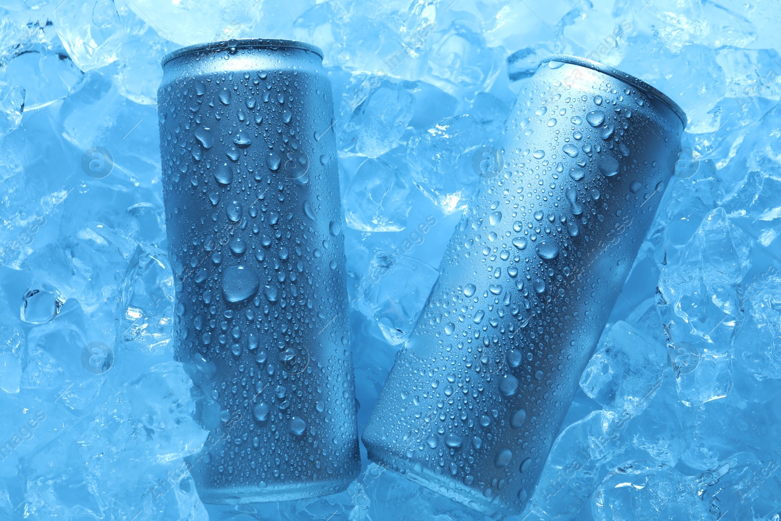 Refreshing drinks in cans on ice cubes, top view. Toned in blue Photo of Refreshing drinks in cans on ice cubes, top view. Toned in blue