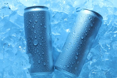 Photo of Refreshing drinks in cans on ice cubes, top view. Toned in blue