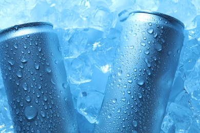 Photo of Refreshing drinks in cans on ice cubes, top view. Toned in blue