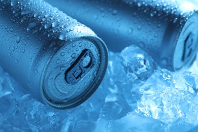 Photo of Refreshing drinks in cans on ice cubes, closeup. Toned in blue