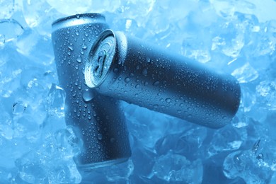 Photo of Refreshing drinks in cans on ice cubes, top view. Toned in blue