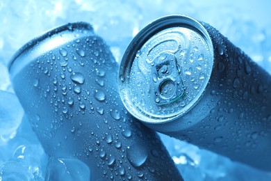 Photo of Refreshing drinks in cans on ice cubes, closeup. Toned in blue