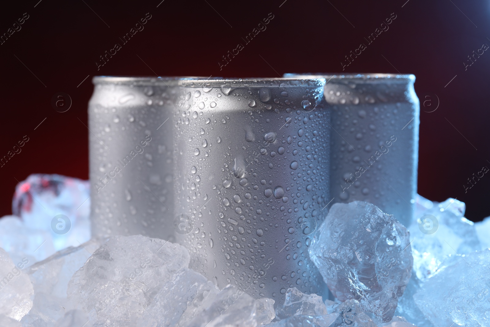 Refreshing drinks in cans on ice cubes against dark red background, closeup Photo of Refreshing drinks in cans on ice cubes against dark red background, closeup