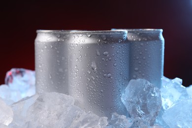 Photo of Refreshing drinks in cans on ice cubes against dark red background, closeup