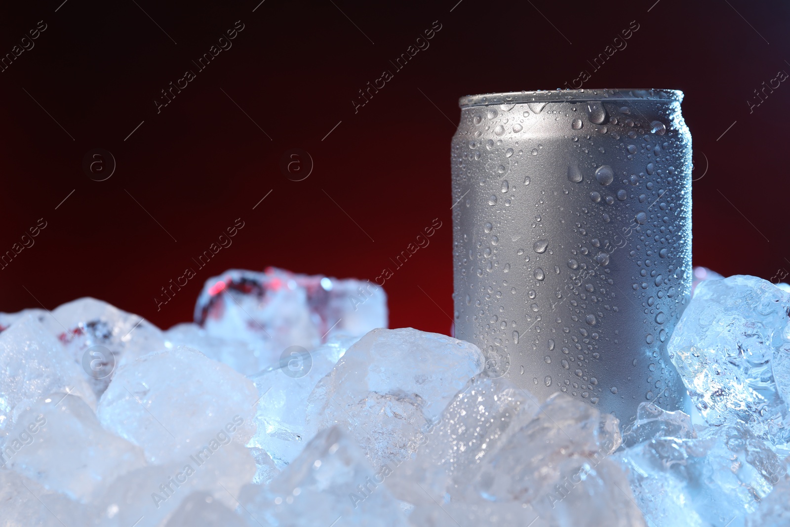 Refreshing drink in can on ice cubes against dark red background, closeup Photo of Refreshing drink in can on ice cubes against dark red background, closeup