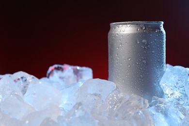 Photo of Refreshing drink in can on ice cubes against dark red background, closeup