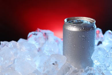 Photo of Refreshing drink in can on ice cubes against dark red background, closeup