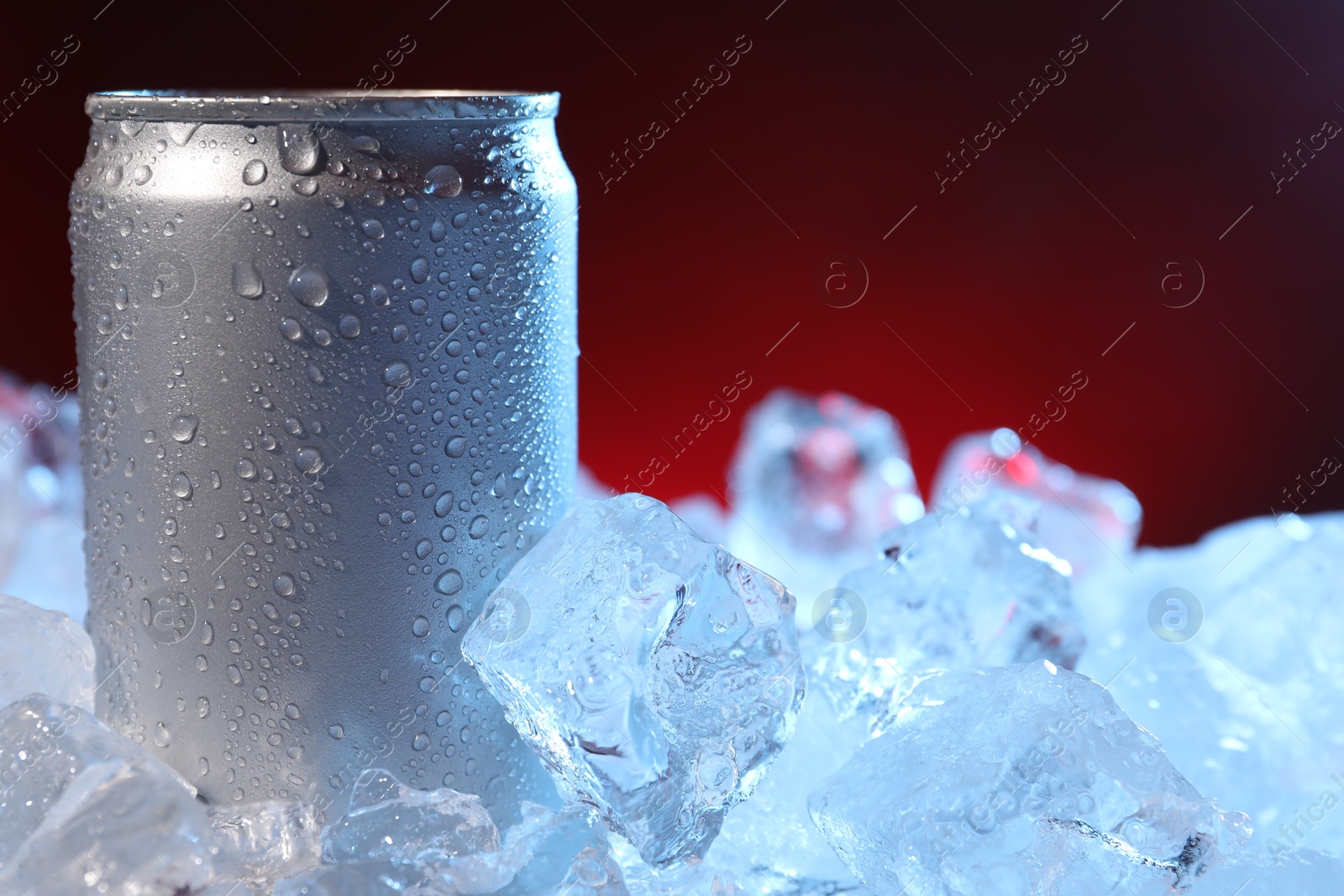Refreshing drink in can on ice cubes against dark red background, closeup Photo of Refreshing drink in can on ice cubes against dark red background, closeup