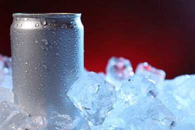 Photo of Refreshing drink in can on ice cubes against dark red background, closeup