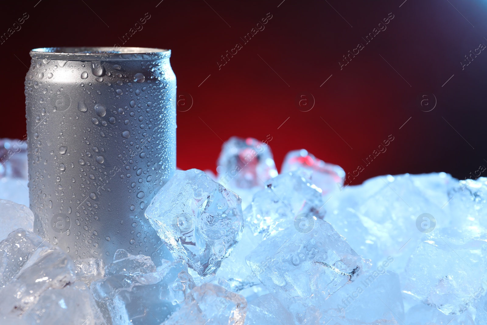 Refreshing drink in can on ice cubes against dark red background, closeup Photo of Refreshing drink in can on ice cubes against dark red background, closeup
