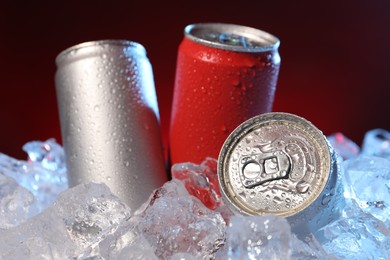 Photo of Refreshing drinks in cans on ice cubes against dark red background, closeup