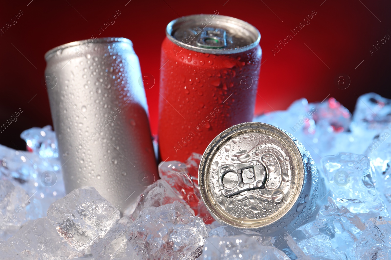 Refreshing drinks in cans on ice cubes against dark red background, closeup Photo of Refreshing drinks in cans on ice cubes against dark red background, closeup