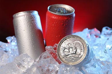 Photo of Refreshing drinks in cans on ice cubes against dark red background, closeup
