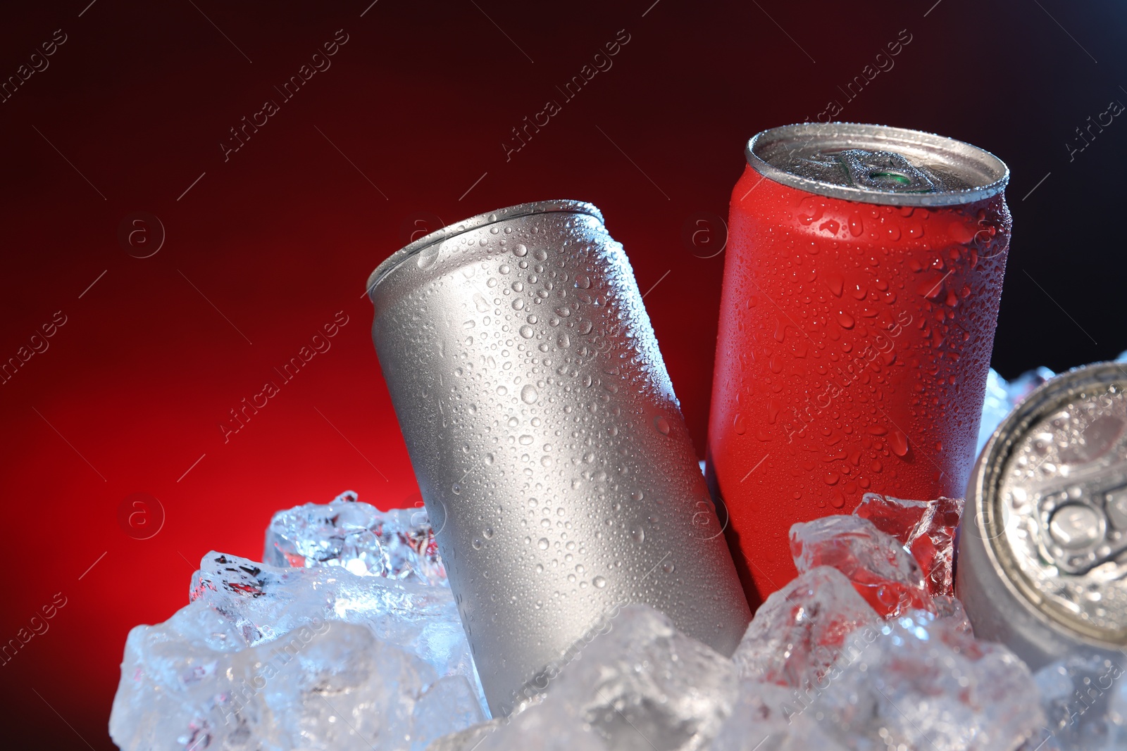 Refreshing drinks in cans on ice cubes against dark red background, closeup Photo of Refreshing drinks in cans on ice cubes against dark red background, closeup
