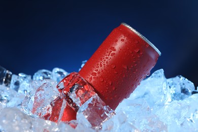 Photo of Refreshing drink in can on ice cubes against dark blue background, closeup