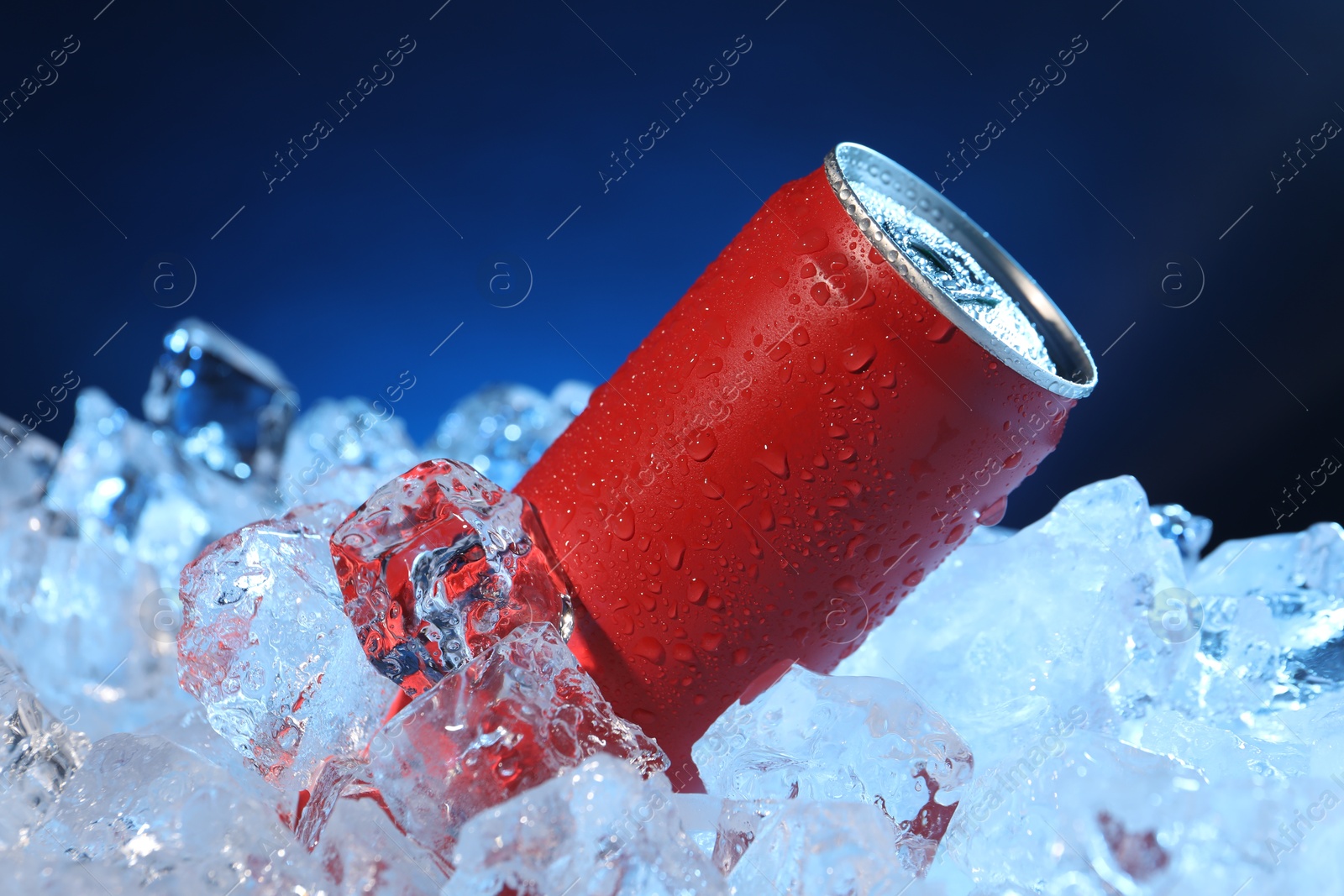 Refreshing drink in can on ice cubes against dark blue background, closeup Photo of Refreshing drink in can on ice cubes against dark blue background, closeup