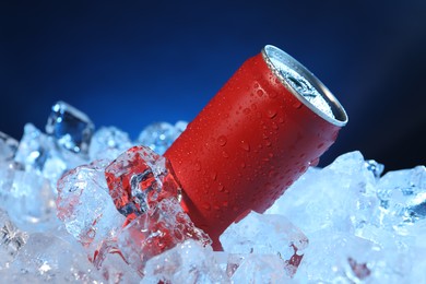 Photo of Refreshing drink in can on ice cubes against dark blue background, closeup