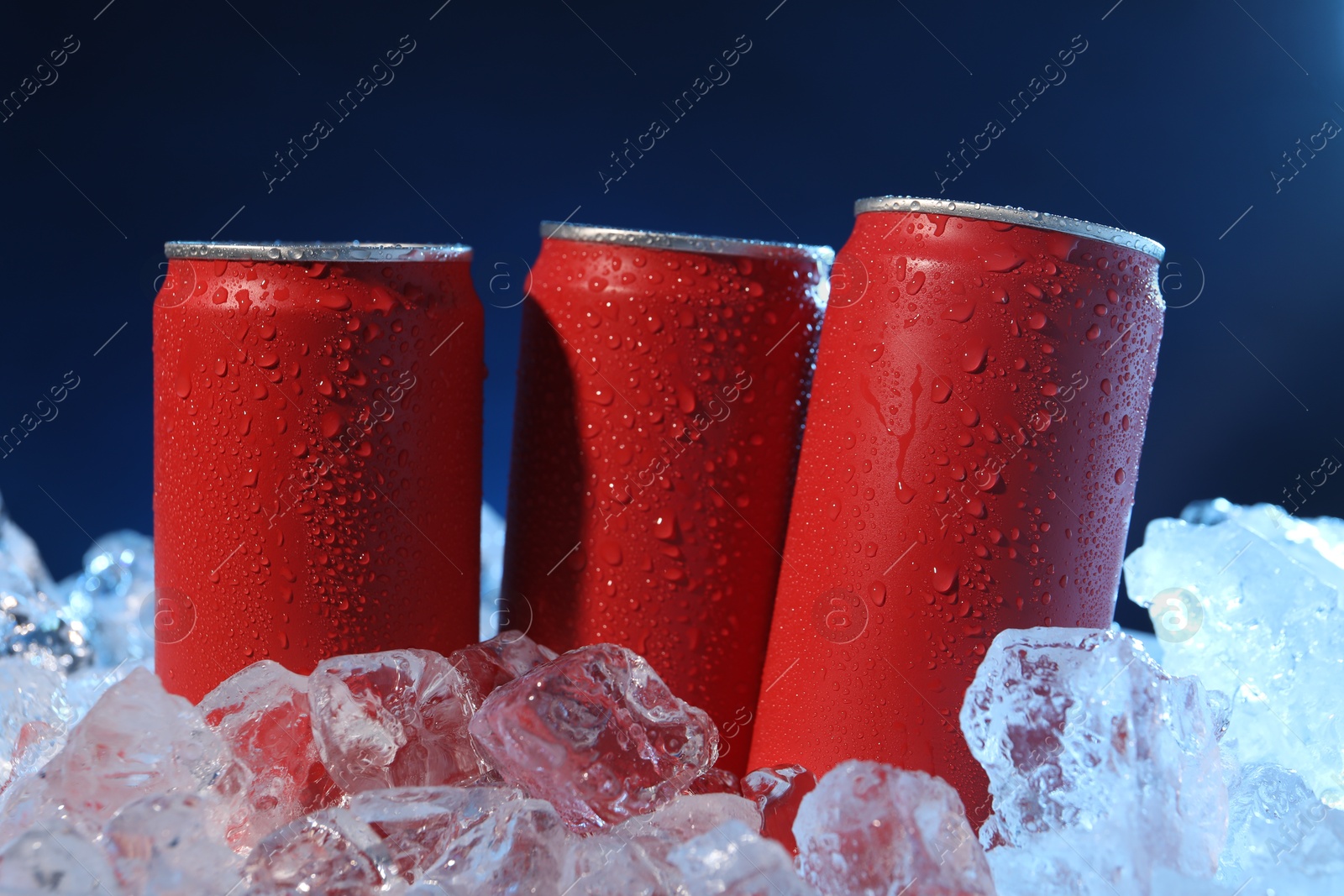 Refreshing drinks in cans on ice cubes against dark blue background, closeup Photo of Refreshing drinks in cans on ice cubes against dark blue background, closeup