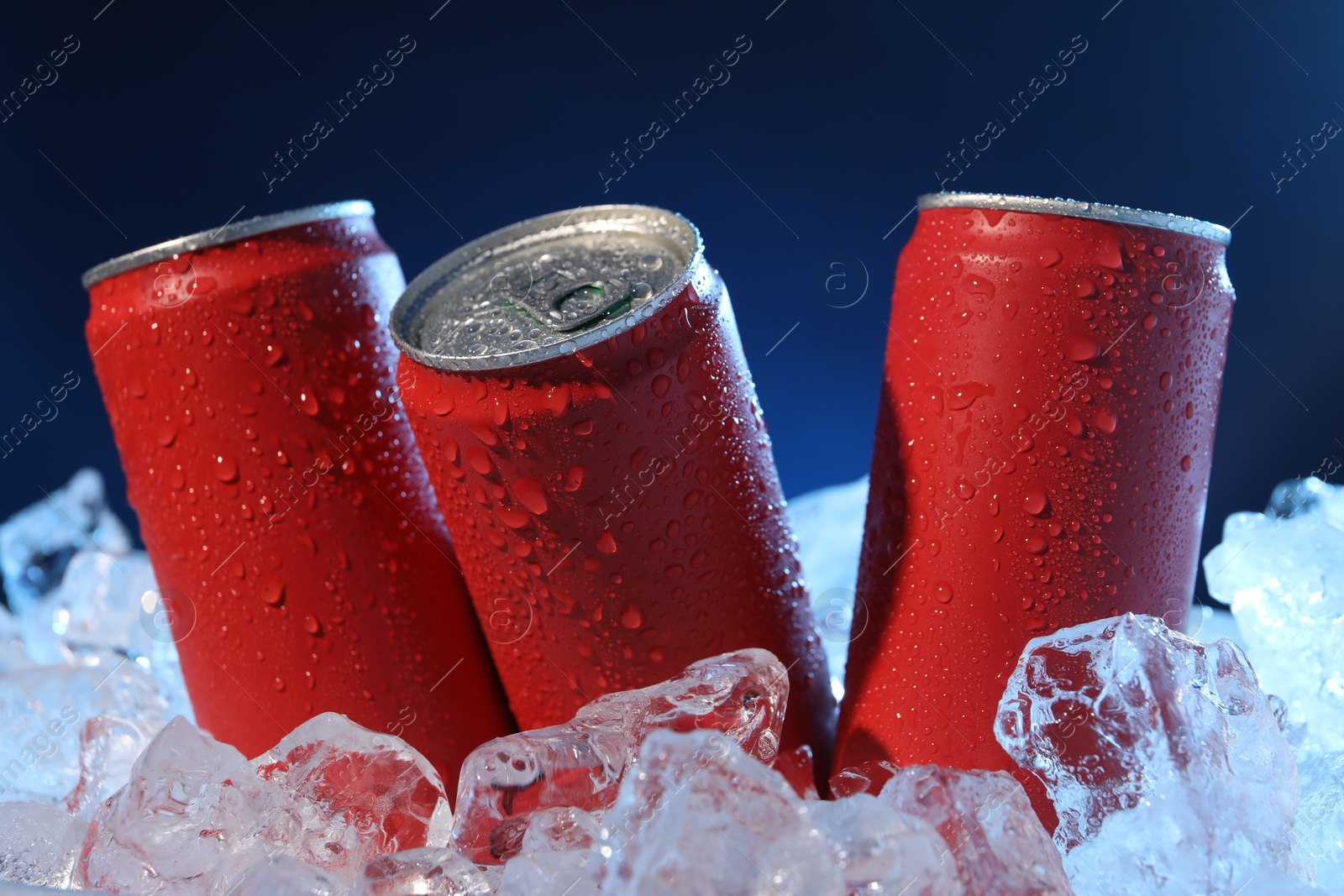 Refreshing drinks in cans on ice cubes against dark blue background, closeup Photo of Refreshing drinks in cans on ice cubes against dark blue background, closeup