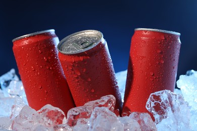 Photo of Refreshing drinks in cans on ice cubes against dark blue background, closeup