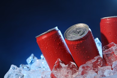 Photo of Refreshing drinks in cans on ice cubes against dark blue background, closeup